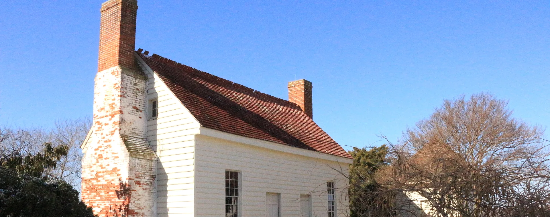 Red-brick chimney rising above the roof of a white clapboard house on a clear cold day