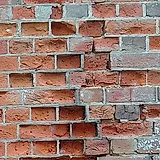 Close-up of brick faces flaking off a red wall