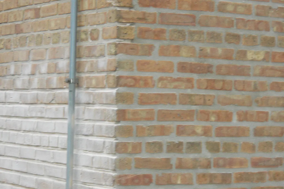 Brick wall corner with freshly refilled mortar joints beside older masonry